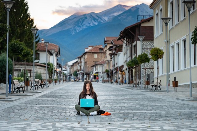 A woman sitting in the middle of an empty street, working on her laptop.